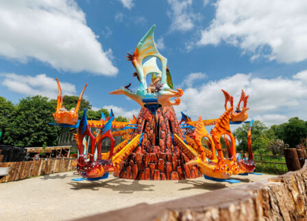 Family enjoying vibrant dragon-themed amusement ride in sunny park setting.