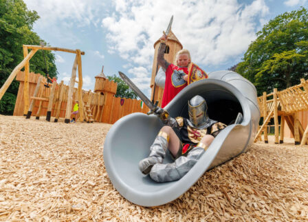 Family enjoying a medieval-themed playground with knights and slides on a sunny day.