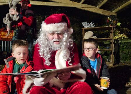 Father Christmas reading to children in a cosy outdoor setting.