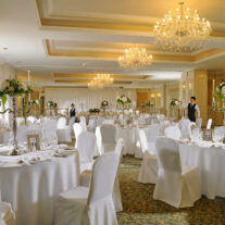 Elegant hotel ballroom set for a wedding reception, with chandeliers and floral centrepieces.