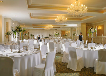 Elegant hotel ballroom set for a wedding reception, with chandeliers and floral centrepieces.