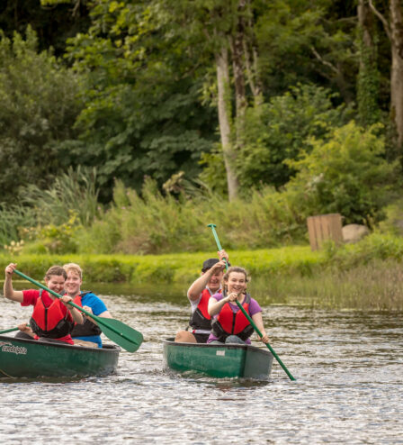 Families canoeing on a serene lake surrounded by lush greenery in a resort setting.