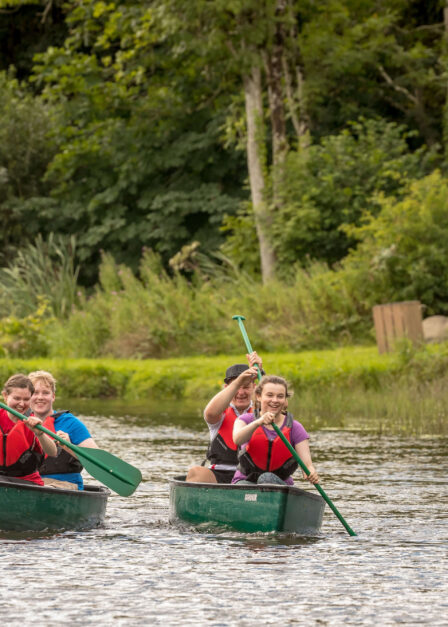 Families canoeing on a serene lake surrounded by lush greenery in a resort setting.
