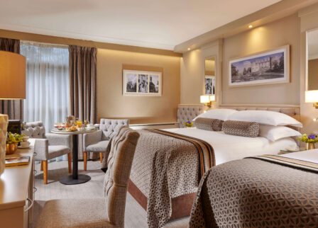 Elegant hotel room with a cosy dining area set for breakfast, warm lighting, and plush bedding.
