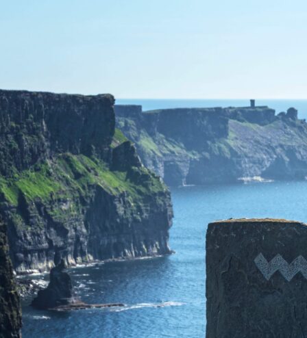 Scenic view of dramatic cliffs by the sea under a clear sky, inviting exploration.