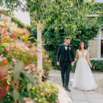 A couple walks hand in hand through a lush, garden path at a charming hotel.