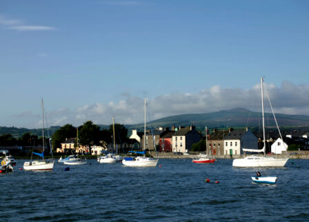 Scenic harbour with sailboats and charming town, set against a backdrop of rolling hills.