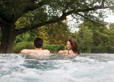 Couple relaxing in a bubbling outdoor pool surrounded by lush greenery.