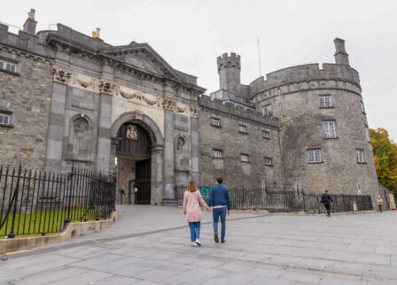 A couple walks hand-in-hand towards a historic stone castle, evoking a sense of adventure.