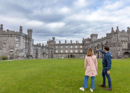 Couple admiring historic castle exterior on a cloudy day.