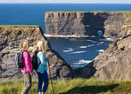 Couple enjoying coastal cliff view with walking sticks on a sunny day.