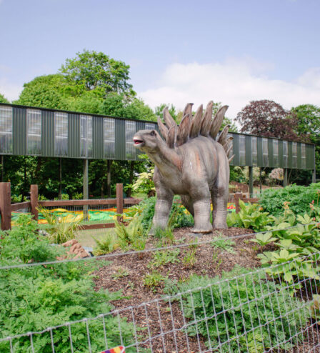 Family exploring dinosaur park at resort, lush greenery, Stegosaurus sculpture.