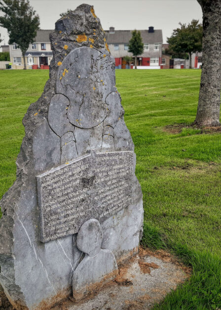 Stone monument with engraved text in a grassy urban park.