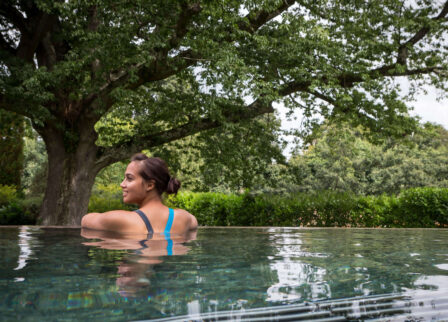 Woman relaxing in a serene outdoor pool surrounded by lush greenery.