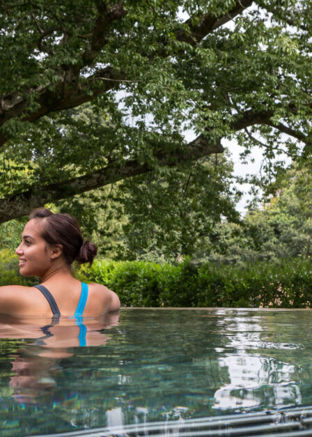 Woman relaxing in a serene outdoor pool surrounded by lush greenery.