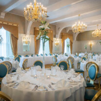 Elegant hotel dining room set for a family gathering with ornate decor and chandeliers.