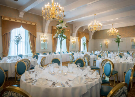 Elegant hotel dining room set for a family gathering with ornate decor and chandeliers.