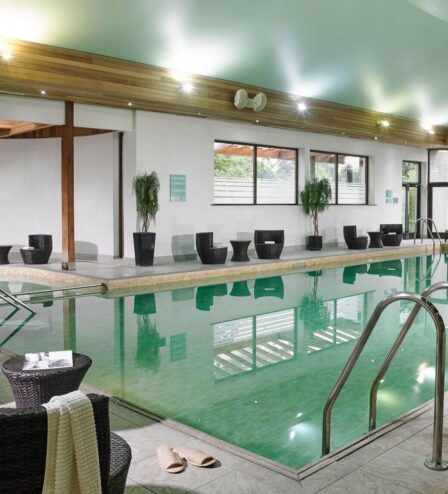 Indoor hotel pool with seating, plants, and warm lighting for relaxation.