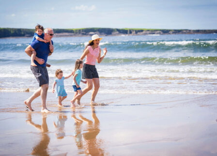 Family enjoying a sunny day at the beach, walking barefoot by the sea.