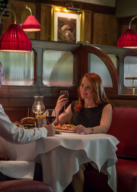 A couple enjoys a cosy dinner at a warm, elegant restaurant with red leather seating.