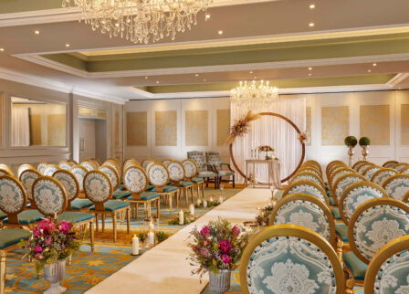 Elegant hotel event room with ornate chairs, floral arrangements, and a large chandelier.