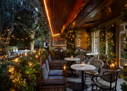 Cosy outdoor restaurant lit with warm string lights and surrounded by lush greenery.