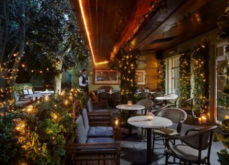 Cosy, candlelit hotel terrace with seated couple and waiter.