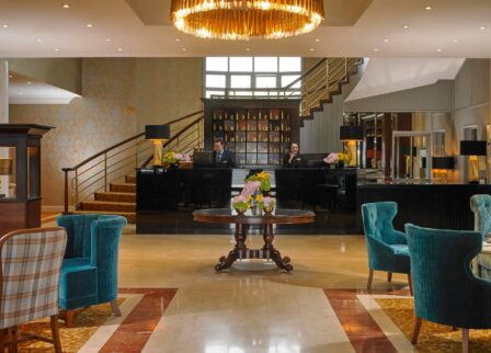 Elegant hotel lobby with warm lighting, plush seating, and two guests checking in at the reception.